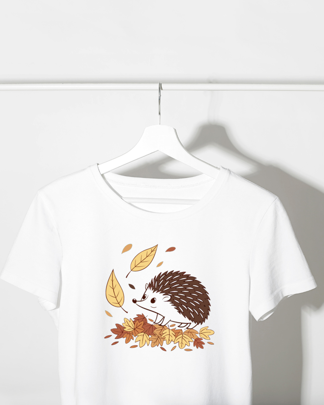 Un t-shirt affichant un hérisson curieux parmi des feuilles d'automne pastel